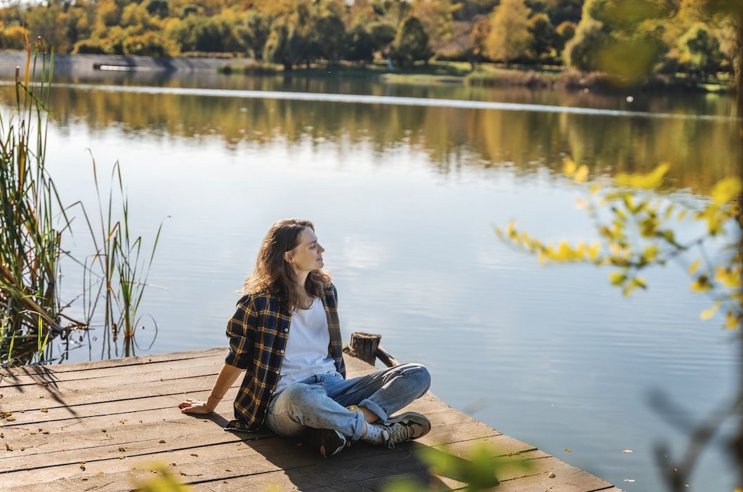 Woman relaxing by a scenic lake during fall RV camping near lake.