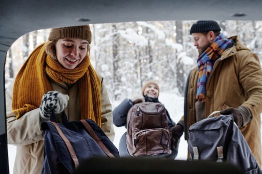 Family unloading luggage from their car during a winter getaway, preparing for a cozy holiday cabin stay.