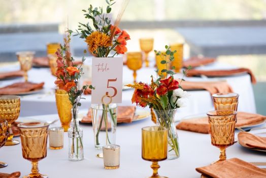 Elegant fall wedding table décor with amber glassware, orange florals, and seasonal centerpieces at an outdoor venue.
