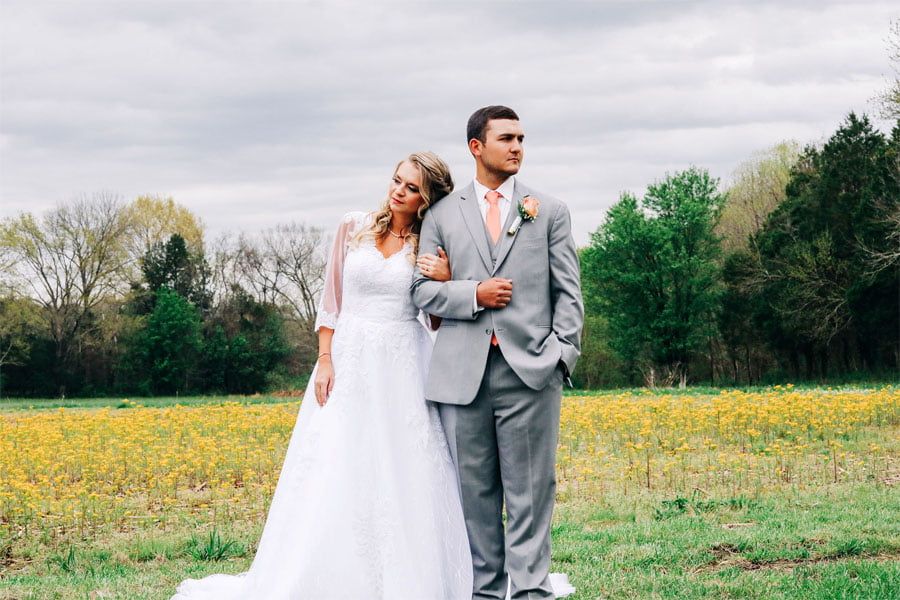 Bride and groom standing in a scenic outdoor field at Rural Hill Farm, an outdoor wedding venue, surrounded by trees and wildflowers.
