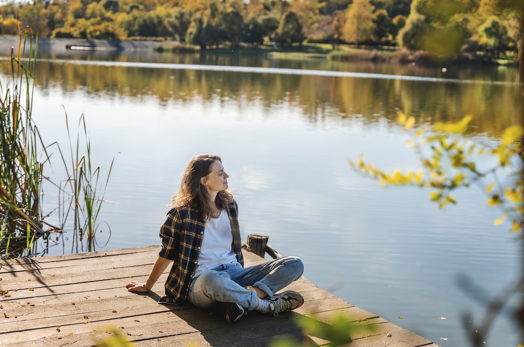 Woman relaxing by a scenic lake during fall RV camping near lake.