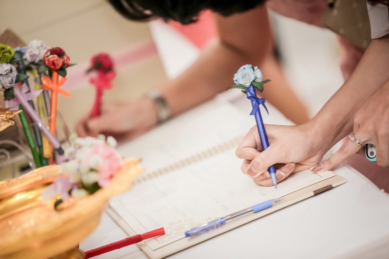 Guest signing a wedding guest book with floral pen at a wedding – creative wedding guest book ideas.
