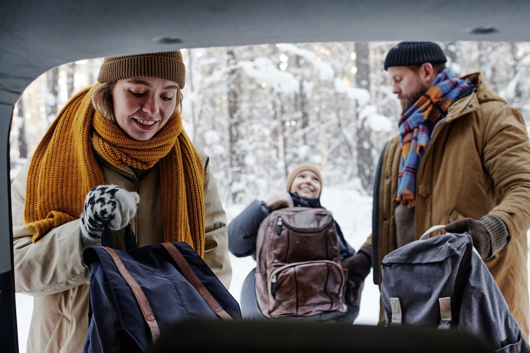 Family unloading luggage from their car during a winter getaway, preparing for a cozy holiday cabin stay.