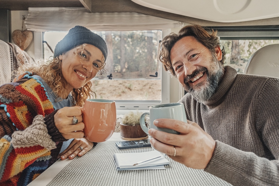 Couple enjoying hot drinks inside a cozy RV during a winter camping trip.