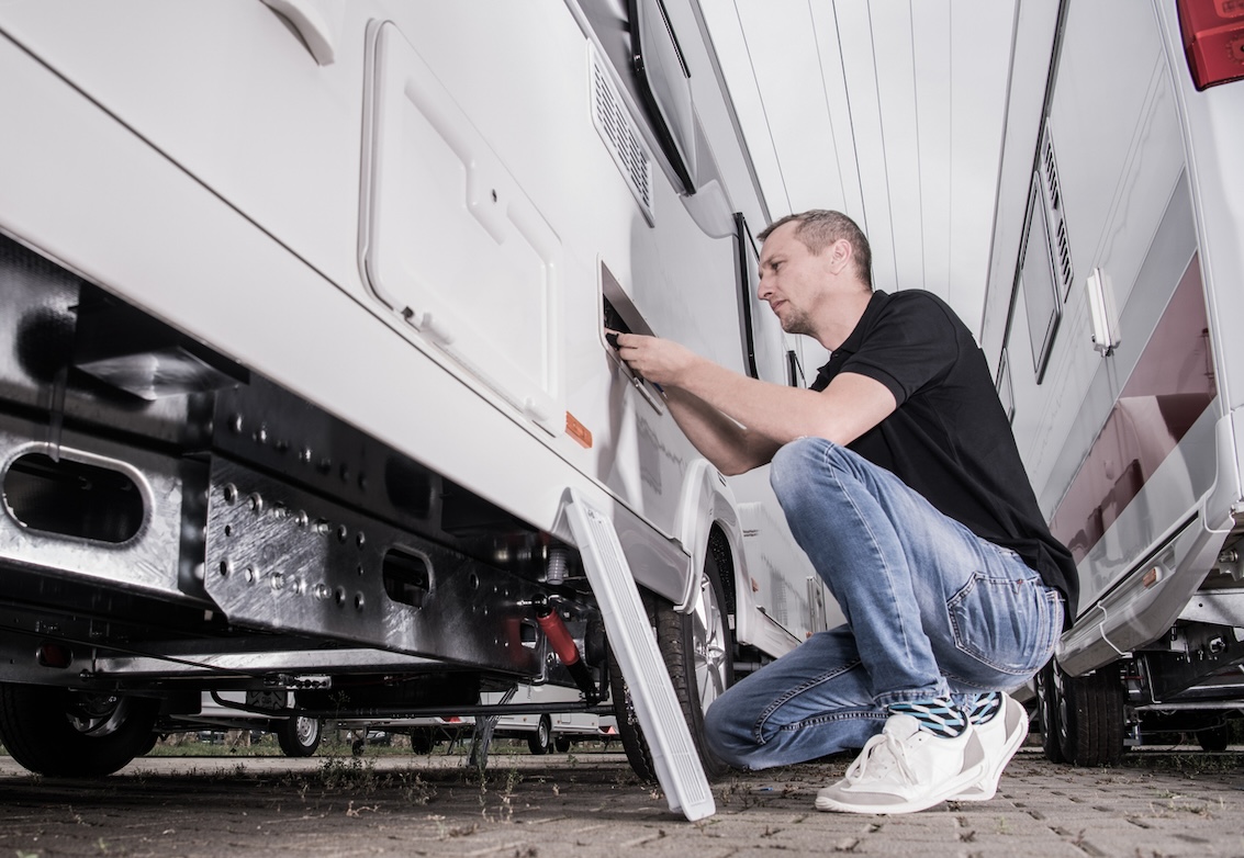 RV owner performing routine maintenance on a travel trailer as part of a seasonal RV maintenance schedule.