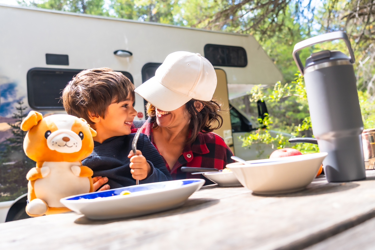 Mother and child enjoying breakfast outside RV at campsite, family RV camping experience with kids