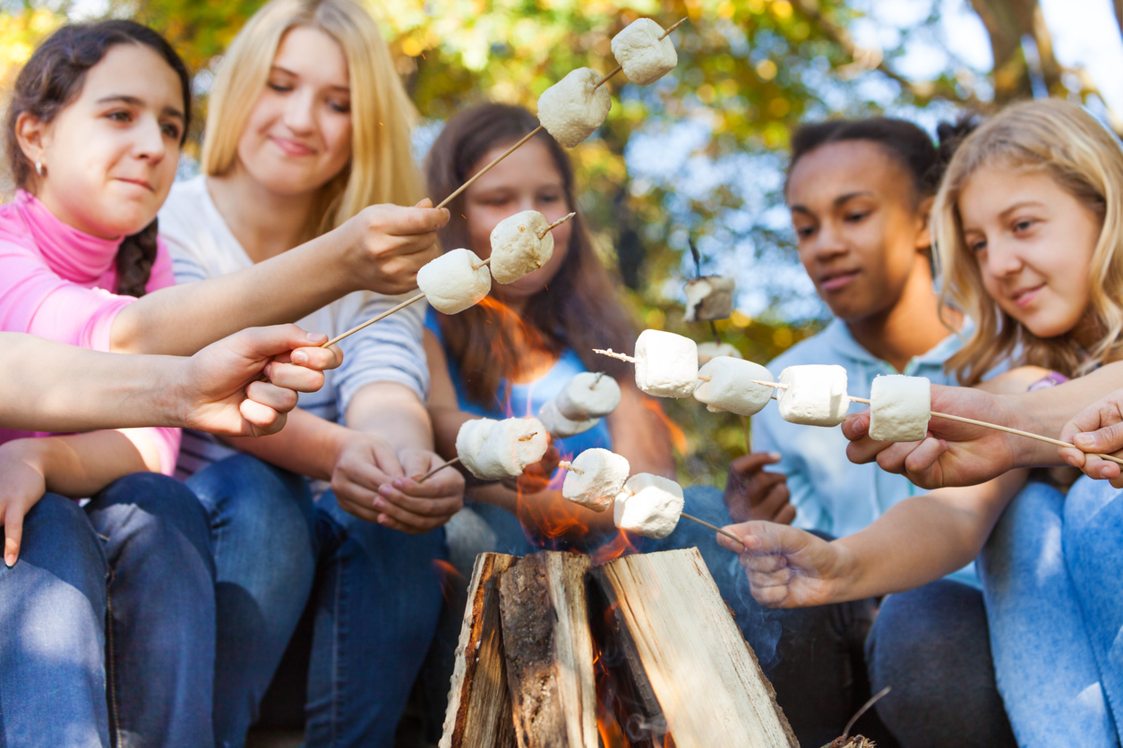 Group roasting marshmallows around a campfire during a camping getaway.