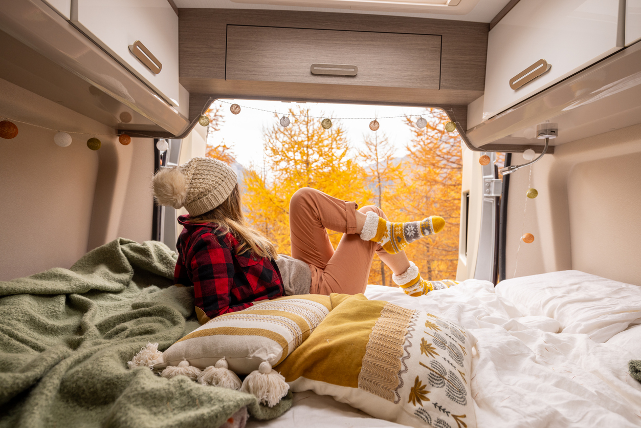 Woman relaxing inside a camper while enjoying colorful fall scenery