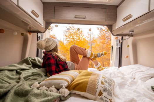 Woman relaxing inside a camper while enjoying colorful fall scenery