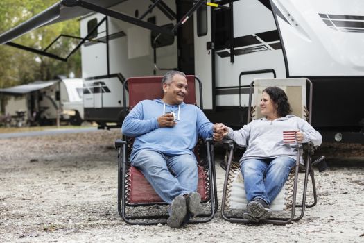 Couple relaxing outside RV at campground with chairs and coffee