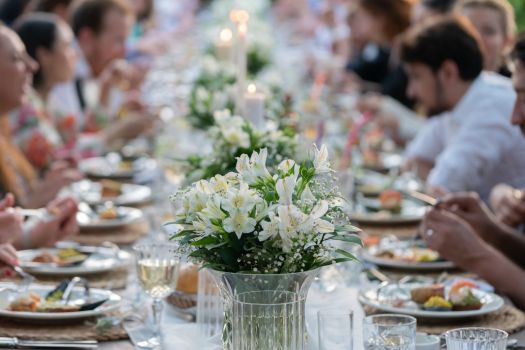 Outdoor wedding reception dinner with guests seated at long table enjoying plated meal and floral centerpiece