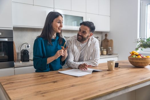 Engaged couple planning wedding at home, reviewing checklist and timeline together in kitchen