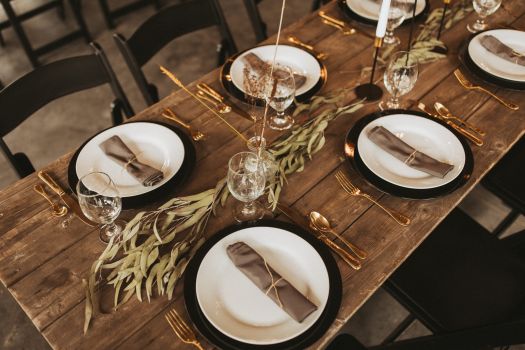 Rustic wedding table setting with elegant place settings, greenery, and gold flatware on a wooden table.